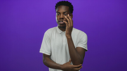 Young man with hand on chin standing thoughtfully before a vibrant purple studio backdrop; reflection.