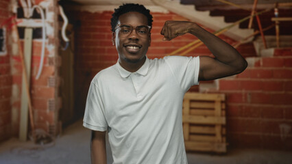 Young african american man flexes arm and points finger to bicep in building interior under...