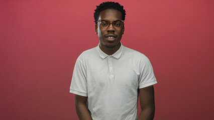 Young african american man wearing glasses stands with closed eyes in a red studio environment;...