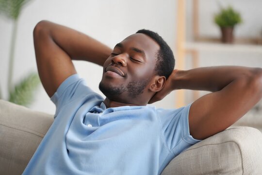 Relaxed african american man resting on sofa at home for stress relief - Powered by Adobe