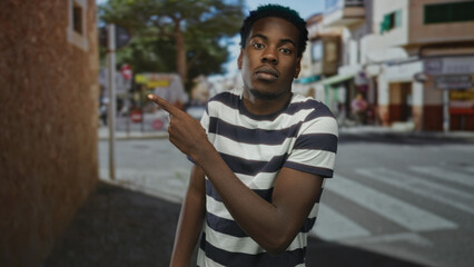 Fototapeta premium Man in striped shirt pointing finger toward crosswalk on bustling street by building wall; attention guidance.