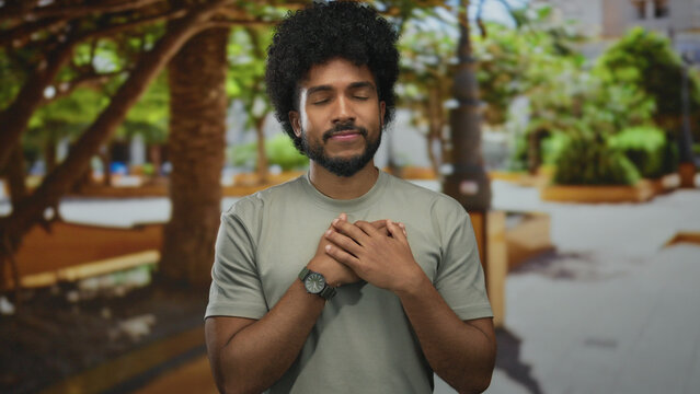 African american man expressing gratitude in a green outdoor park on a sunny day, showcasing a heartfelt gesture.