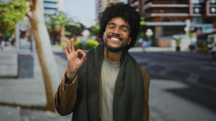 Smiling man in city street gives okay gesture, exuding positivity and happiness in an urban outdoor...