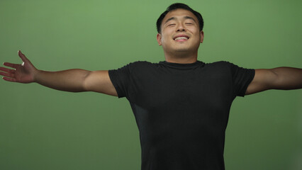 Man spreads arms in green studio setting, head thrown back with broad smile and chest forward as he embraces the space; freedom.