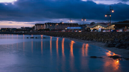 Salthill Promenade sunset seascape in Galway, Ireland, a romantic nightscape illuminated by street lights and buildings at the charming coastal village on the North Atlantic Ocean.