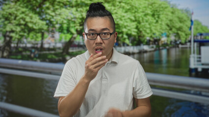 Man with hands covering mouth on a street bridge over a canal in amsterdam; anxiety unease hesitation.
