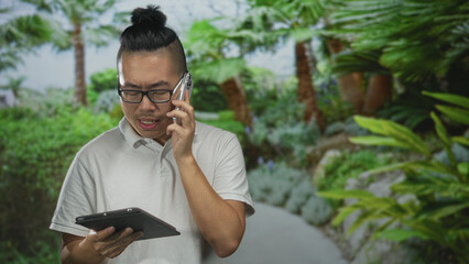 Man holding tablet with one hand and phone to ear in forest path, glancing at device screen while standing; problem solving concern.
