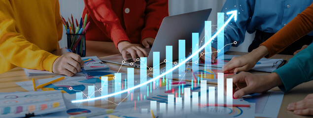 A business team collaborates at a modern workspace, analyzing data trends with graphs and charts while using a laptop to enhance financial growth strategy. Scalp