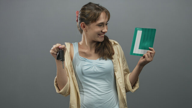 Woman smiling while holding car keys and green learner plate in grey studio, showing relaxed pose and casual shirt; pride new driver. - Powered by Adobe