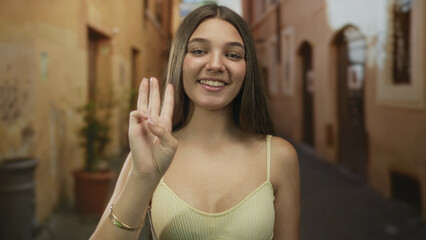 Caucasian teenage girl with raised hand holds up four fingers on a sunlit old town street; youthful optimism.