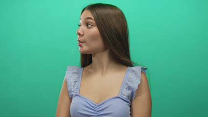 Caucasian teen girl in lavender top puckers lips and raises eyebrows in green studio with direct...