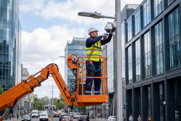 Professional technician installing security camera on street pole from hydraulic lift bucket in modern city center