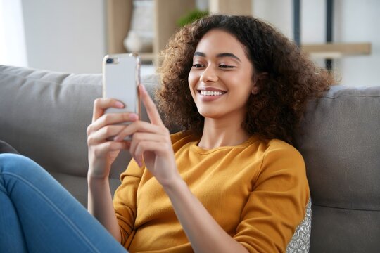 Smiling woman using smartphone at home browsing social media on couch sofa - Powered by Adobe