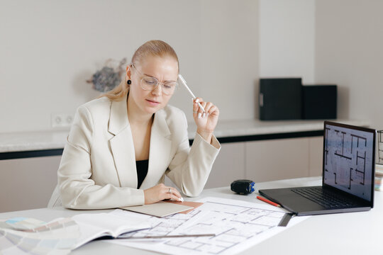 Concentrated interior designer caucasian female architect reviewing blueprints at office desk