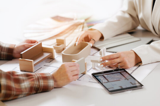 Hands building architectural model with plans and tablet in professional setting, design project of interior