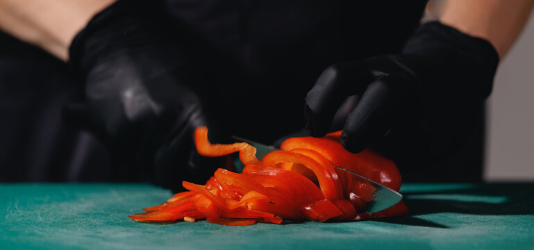 Caucasian adult slicing red bell pepper with black gloves on cutting board