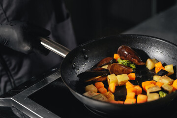 Chef cooking mussels and vegetables in pan on stove, top view