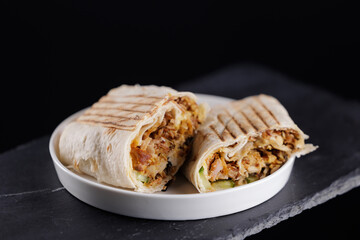 Closeup Delicious grilled chicken wrap shawarma halves on slate plate against black background