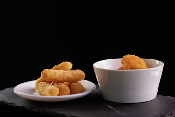 Breaded mozzarella sticks and nuggets on black slate background