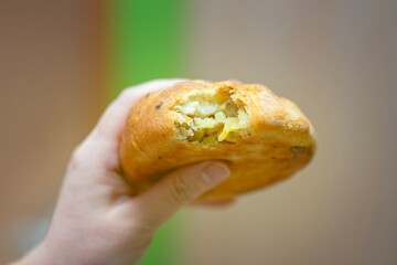 Woman's hand holding a bitten pastry elesh filled with potato and meat