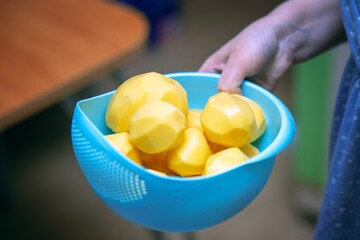 Woman's hand carrying a blue plastic bowl filled with peeled potatoes