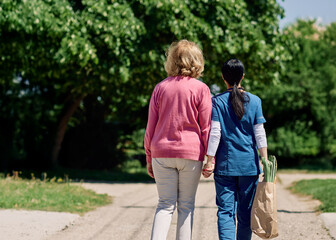 Obraz premium Nurse caregiver with senior woman walking outdoors and helping with shopping bag with groceries