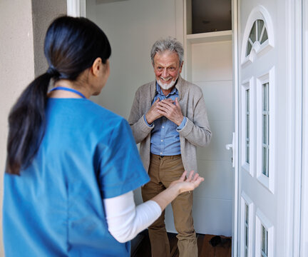 Doctor or nurse caregiver woman with senior man at home or nursing home, a caregiver standing on the front door arriving and being welcomed by a senior man - Powered by Adobe