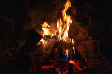 A glowing campfire burns among rocks, casting amber light and blue flames
