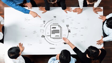 A diverse team engages in a collaborative business meeting, analyzing project workflow on a table filled with documents, ideas, and technology icons. Raster