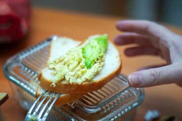 Teen's hand reaching for a homemade avocado sandwich during breakfast time