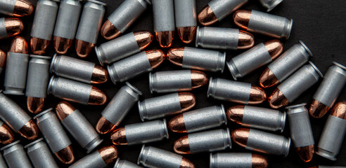 A close-up, top-down view of a dense pile of silver-cased pistol cartridges on a dark back