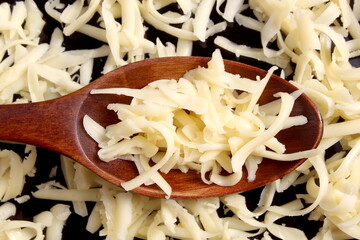 There is a spoon with grated cheese on a black background.	