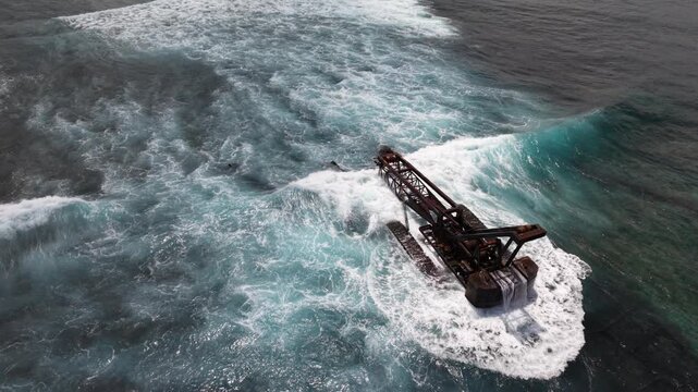 Escavator wreck sea coast with waves of Bali, Nusa Lembongan Island drone aerial shot in Indonesia surrounded by beautiful jungle and tropical blue sea water and cliffs
