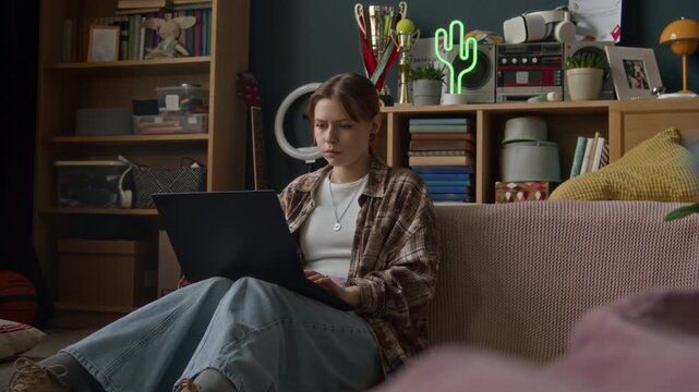 Zoom in shot of focused young Caucasian female zoomer studying on wireless laptop in cozy room