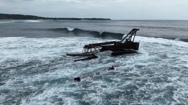 Escavator wreck sea coast with waves of Bali, Nusa Lembongan Island drone aerial shot in Indonesia surrounded by beautiful jungle and tropical blue sea water and cliffs