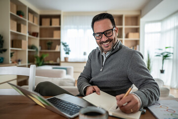 Smiling man working from home, planning tasks in notebook