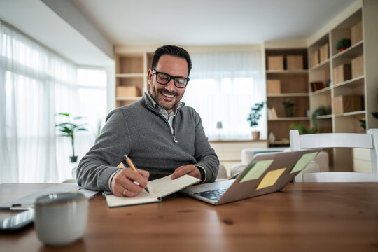 Smiling man planning schedule writing notes working from home