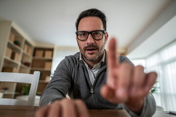Man in glasses pointing during video call at home