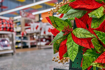 Vibrant Christmas decorations featuring red and green foliage with golden accents in a mall setting, showcasing festive ambiance and ample blurred copy space for text