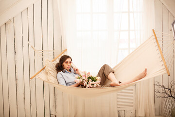 A serene woman relaxes in a hammock, gently holding a bouquet of flowers. The scene evokes tranquility, relaxation, and beauty. Ideal for content related to wellbeing, nature, or gifts.