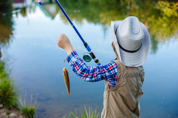 A person enjoys fishing on a tranquil lake, equipped with a blue rod and wearing a hat. Captures a...