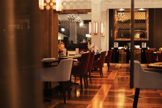 An elegant luxury restaurant dining room interior with plush red and white chairs, warm lighting, and glossy wood flooring.