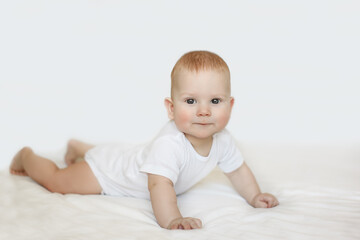 A charming baby boy with vibrant red hair rests on his stomach, gazing upwards with a curious and innocent expression. The white background emphasizes the baby's features.