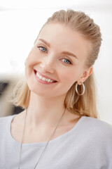 Naklejka premium A beautiful blonde woman smiles warmly, wearing a casual gray top and large hoop earrings. A joyful and inviting portrait.