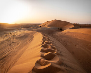 Golden desert sand dunes with footprints under a clear sky at sunset landscape nature