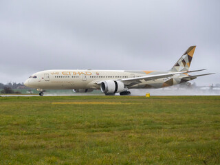 Naklejka premium PRAGUE, Czech Republic - November 17, 2025: Etihad Airways Boeing 787-9 Dreamliner (A6-BLK) taxiing on a wet runway with water spray.