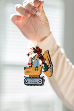 a hand holding an ornament with a yellow bulldozer and a santa claus for christmas time