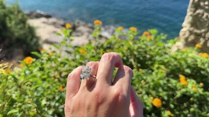 Female hand wearing diamond engagement ring above clear turquoise water, glowing in soft Mediterranean sunlight in Croatia.