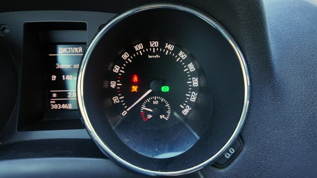 instrument cluster lighting up with speedometer and warning icons during startup, closeup of circular gauge with illuminated indicators and odometer, moody cabin light and textured dial face