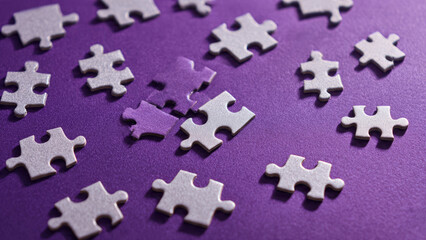 Silver jigsaw puzzle pieces lie scattered on a vibrant purple background, waiting to be assembled, symbolizing challenge and problem-solving.